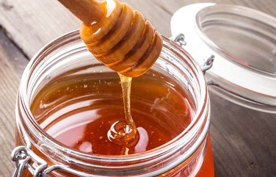 How to Get Rid of Razor Bumps: honey drizzling from honey spoon into glass jar