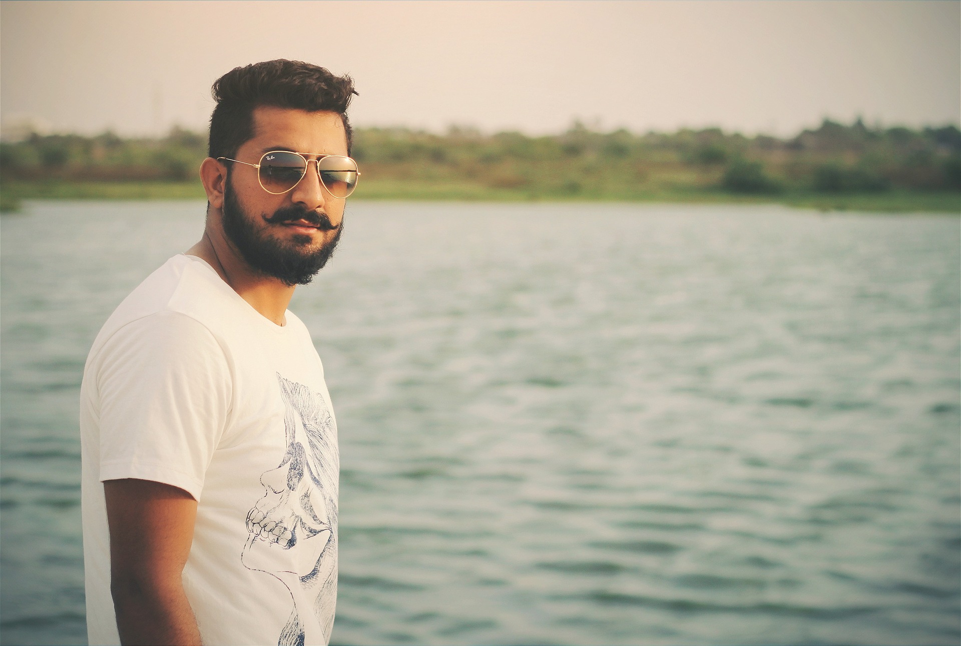 Man wearing shades and has a beautiful beard is standing near the ocean