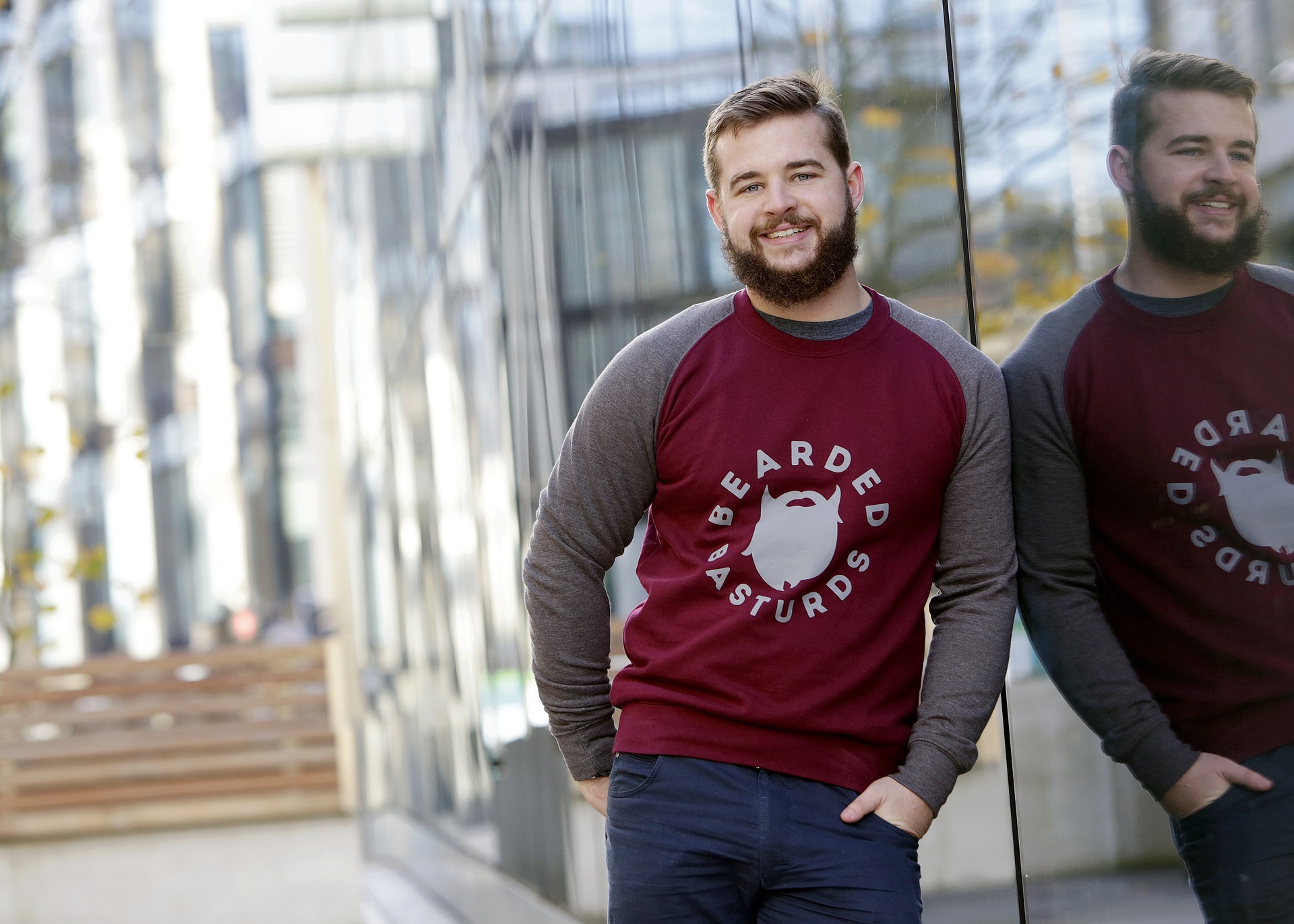 Man with a beautiful beard lying his shoulder to a mirror wall with his reflection on it