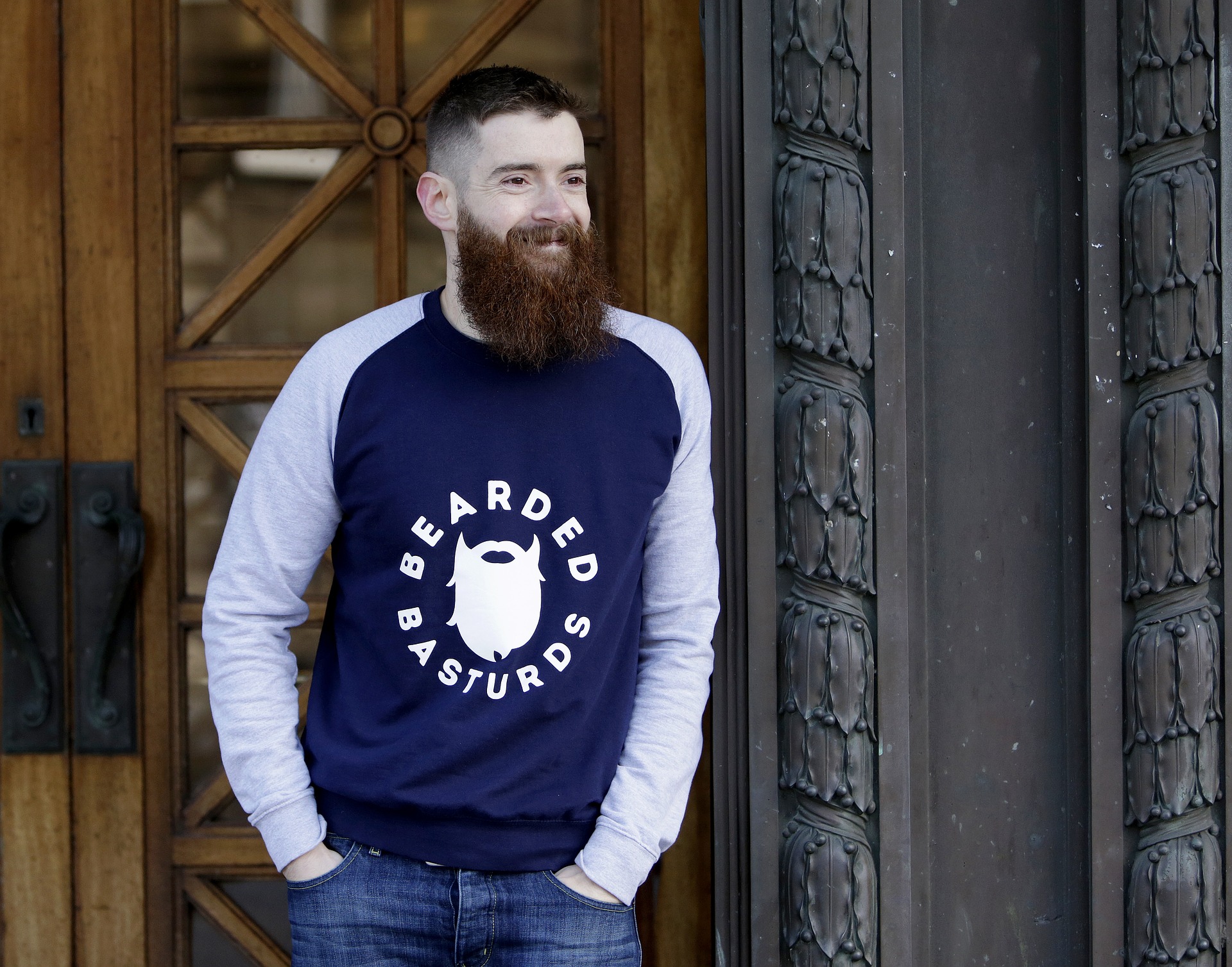 Smiling man with a beautiful beard is standing outside the door