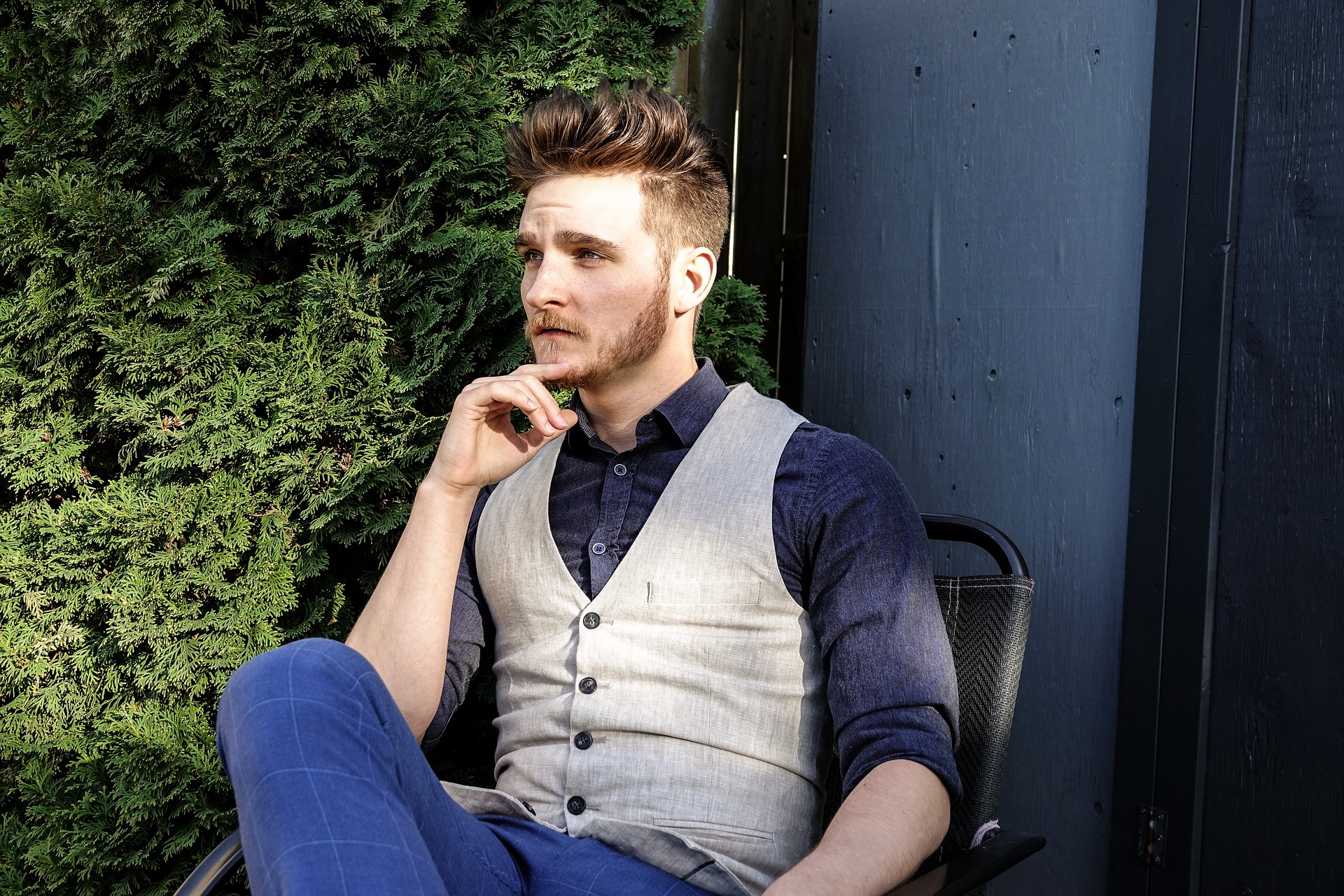 Man with a beautiful beard wearing a work outfit is sitting at the chair 