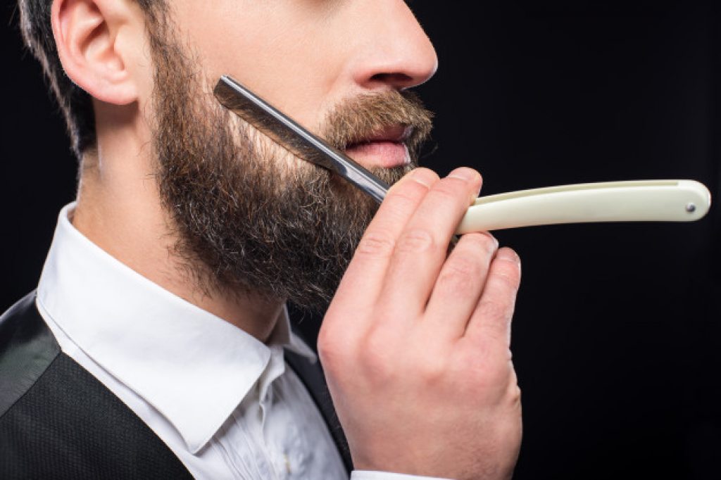 side view of a man shaving himself with a straight razor