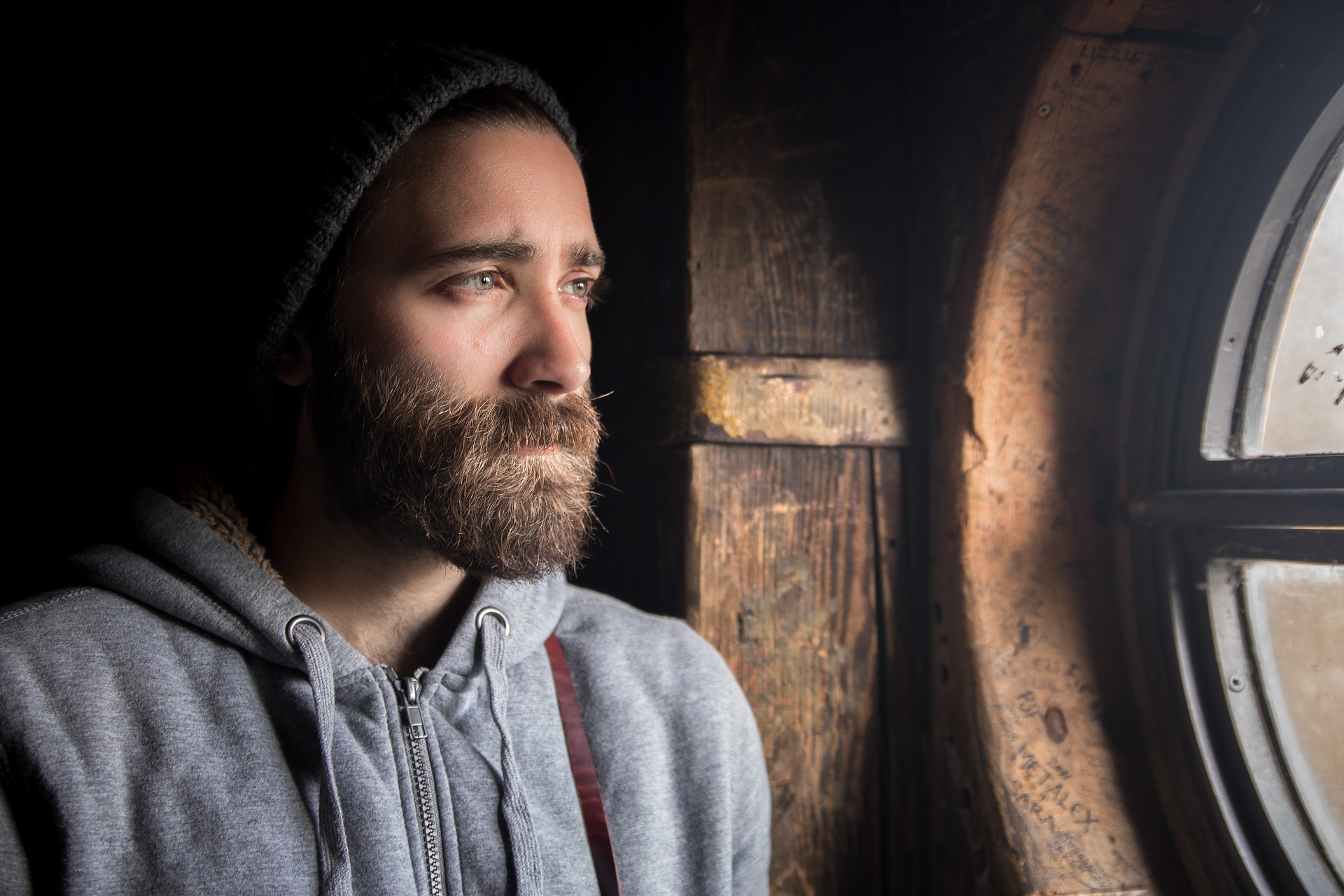 bearded man looking out a window 