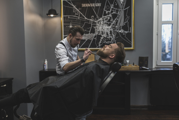 barber trimming beard of customer